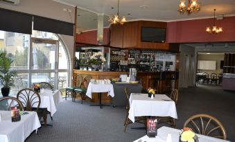 a restaurant with white tablecloths on the tables and chairs , and a bar in the background at Colac Mid City Motor Inn