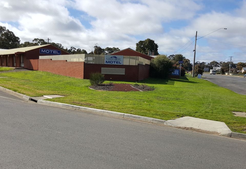 "a brick building with a blue sign that says "" motel "" is surrounded by a green grass area and trees" at Country Road Motel St Arnaud