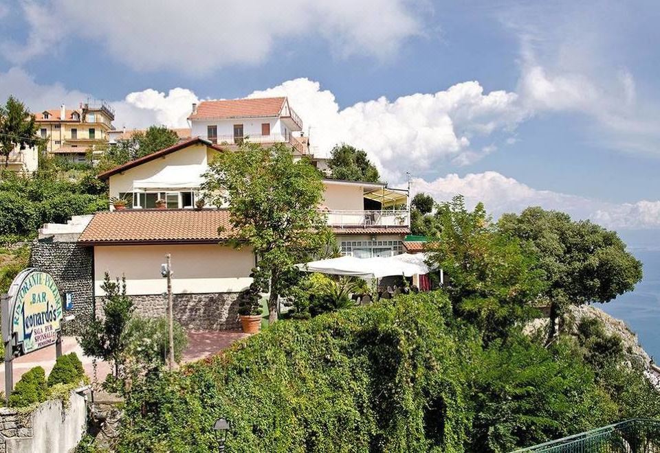 a large house with a red roof is perched on a hillside , overlooking greenery and trees at Leonardo's
