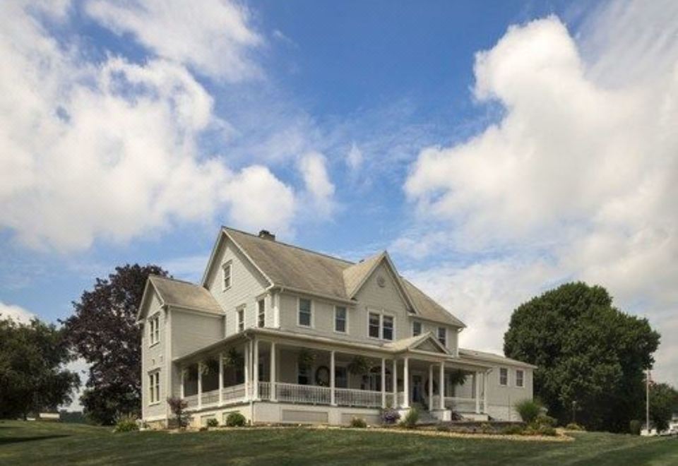 a large white house with a porch and columns is surrounded by a grassy field at The Jacqueline House of Wilmington