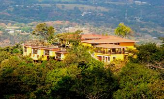 a large building with a balcony is perched on a hillside surrounded by trees and mountains at Barons Resort