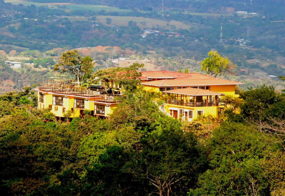 a large building with a balcony is perched on a hillside surrounded by trees and mountains at Barons Resort