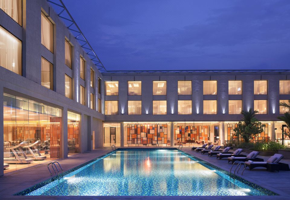 an outdoor swimming pool surrounded by a hotel , with several people enjoying their time in the pool area at Courtyard Kochi Airport