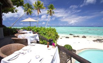 an outdoor dining area with a table set for two people , situated on the beach at Small Luxury Hotels of the World - Pacific Resort Aitutaki