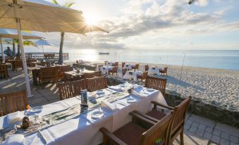 a beach restaurant with tables set up on the sand , chairs , and an umbrella , offering a beautiful view of the ocean at Castaway Island Fiji