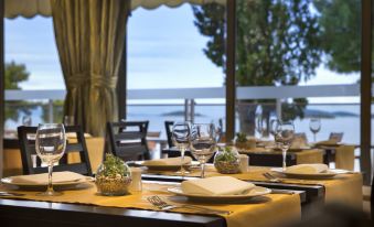 a well - arranged dining table with wine glasses and plates , set for a meal in a restaurant with a view of the ocean at Aminess Grand Azur Hotel