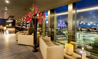 a modern lounge area with a large vase of pink flowers and white couches , overlooking a city skyline at Fletcher Wellness-Hotel Leiden