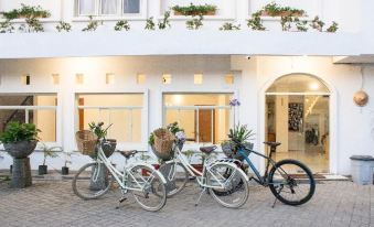 three white bicycles are parked next to each other in front of a white building with potted plants on the sidewalk at Tani Jiwo Hostel