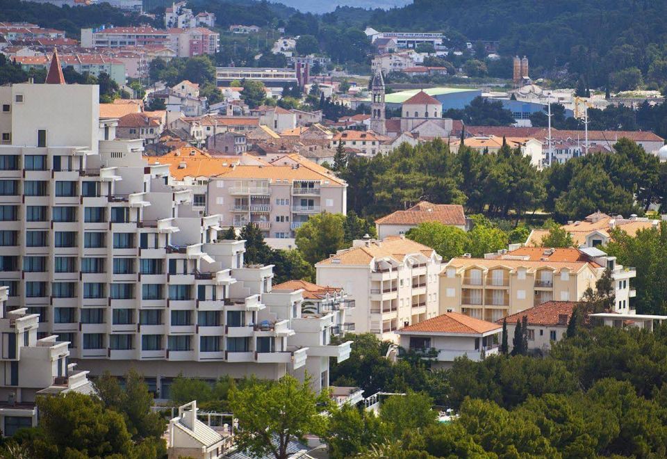 a large white building with a red roof is nestled in the valley , surrounded by trees and mountains at Valamar Meteor Hotel