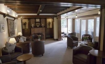 a spacious living room with wooden beams on the ceiling , multiple chairs , and a fireplace at Little Silver Country Hotel