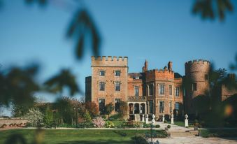 a large , red brick building with a grassy yard and blue sky in the background at Rowton Castle