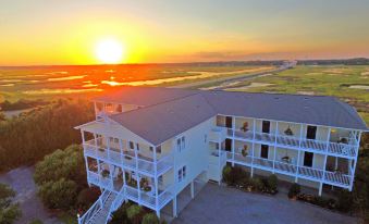 a large white building with a balcony is surrounded by trees and overlooks a sunset over the water at The Sunset Inn