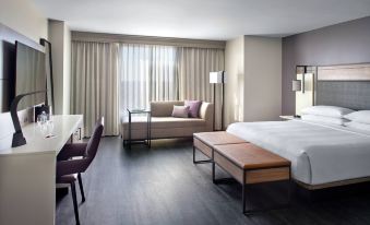 a modern hotel room with wooden floors , white walls , and large windows , featuring a comfortable bed , a couch , and a dining table at Raleigh Marriott City Center