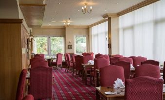a dining room with red chairs and tables , a chandelier hanging from the ceiling , and large windows at Cairn Hotel