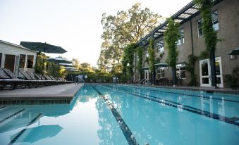 a large outdoor swimming pool surrounded by buildings , with umbrellas and chairs placed around the pool area at Southbridge Napa Valley