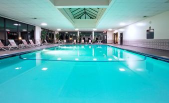 an indoor swimming pool surrounded by chairs and tables , with people enjoying their time in the pool at Holiday Inn Express Big Rapids