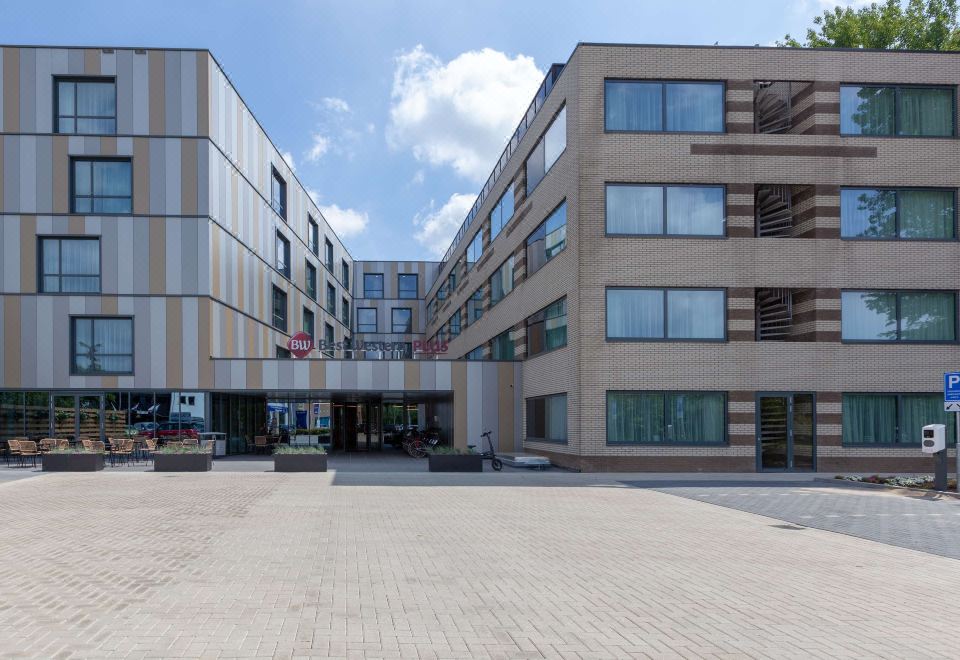 a modern building with multiple floors , surrounded by trees and people walking on the street at Best Western Plus Hotel Amstelveen