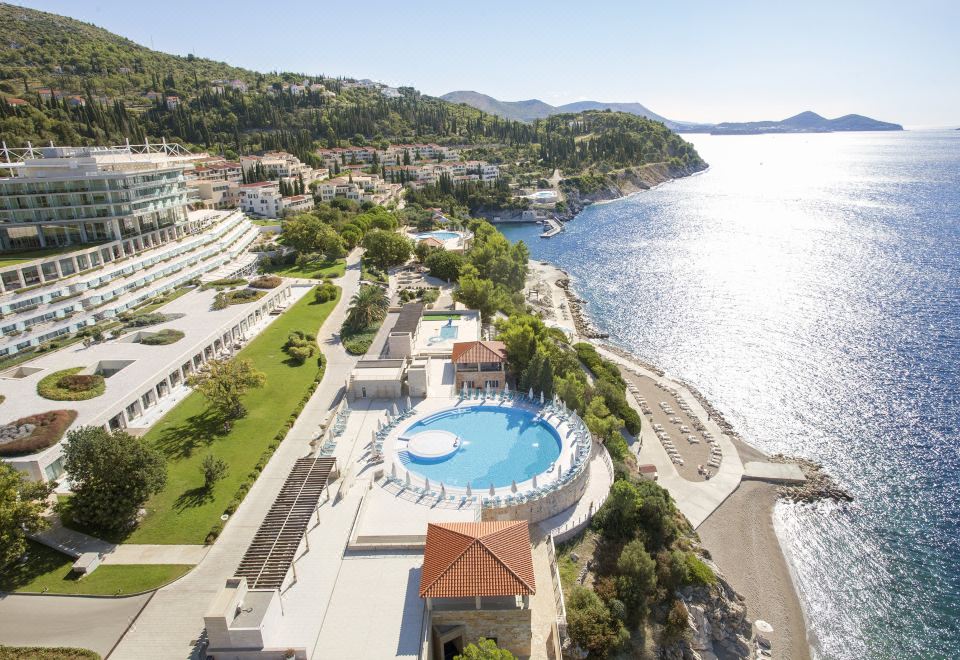 a large swimming pool is surrounded by buildings and trees , with a clear blue sky above at Sun Gardens Dubrovnik