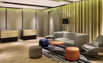 a modern living room with a gray couch , orange and blue ottomans , wooden flooring , and green curtains at Novotel Jakarta Mangga Dua Square