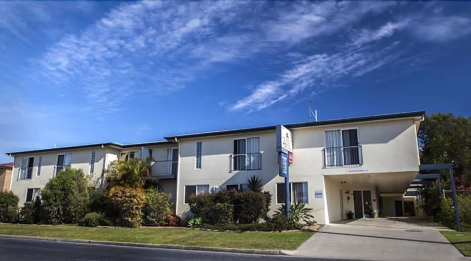 a two - story house with a blue sign and palm trees in front of it under a clear sky at Mandarin Motel