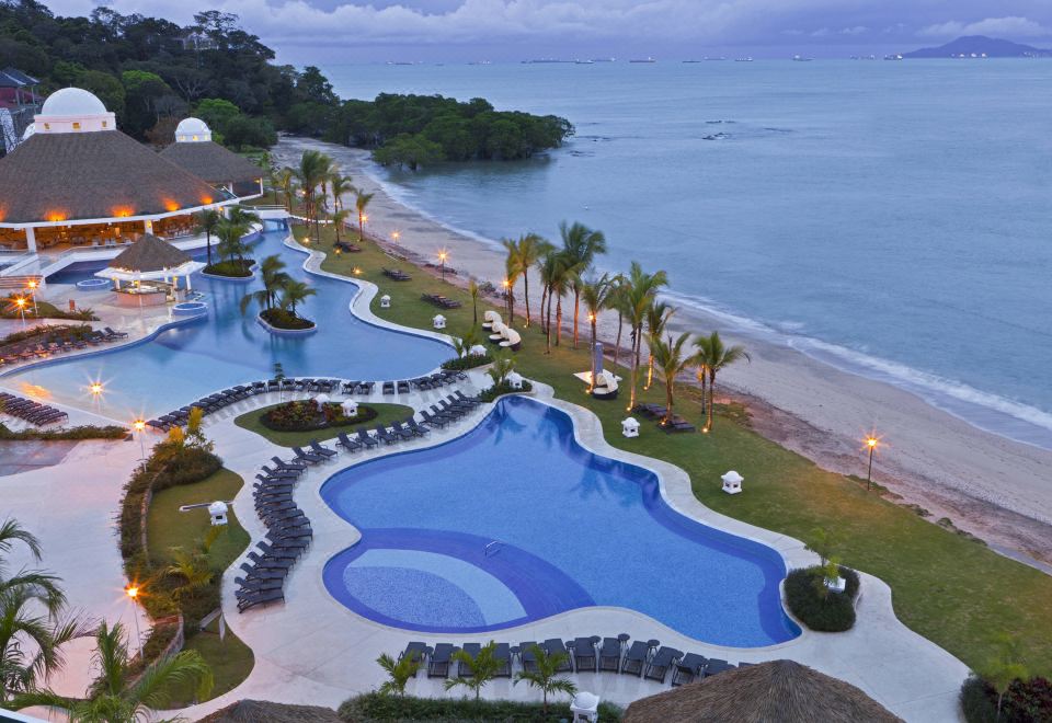 a resort with a large pool surrounded by lounge chairs and palm trees , overlooking the ocean at The Westin Playa Bonita Panama