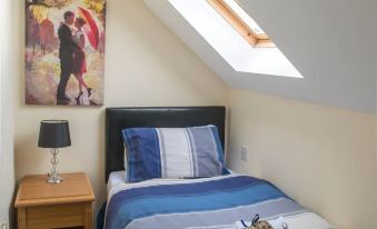 a cozy bedroom with a bed , nightstand , and a painting on the wall , featuring two king - sized beds with blue bedding at The Olde Peculiar