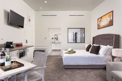 a large , white bedroom with a king - sized bed and a bathroom nearby , connected to a living area at The Swan Valley Retreat