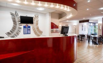 a modern office reception area with a red and white color scheme , equipped with a desk , chairs , and computers at Comfort Hotel Montlucon