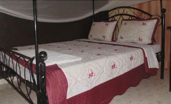 a bed with a white and maroon comforter , surrounded by black metal frames and a headboard at Coronation Hotel