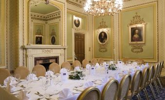a formal dining room with a long table covered in white tablecloths and set for a meal , surrounded by gold chairs at Mercure Blackburn Dunkenhalgh Hotel & Spa