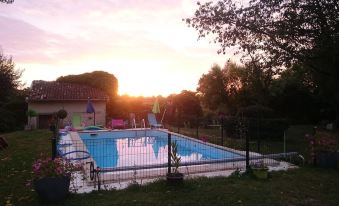 a backyard with a swimming pool surrounded by a fence , and the sun is setting in the background at La Cure