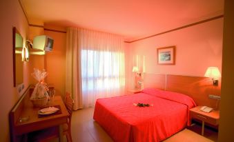 a hotel room with a red bed , curtains , and a television mounted on the wall at Hotel Vent de Mar