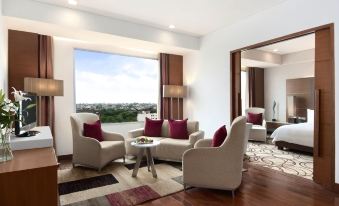 a modern living room with a large window , wooden floor , and white furniture , including two chairs and a coffee table at Hyatt Centric Janakpuri New Delhi