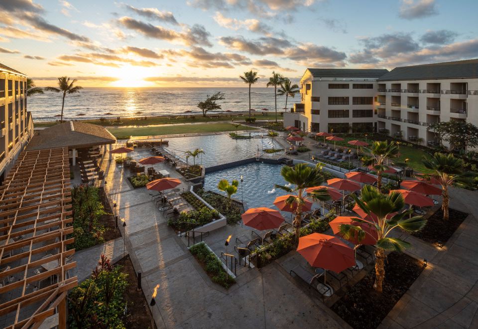 a large resort with a pool , umbrellas , and palm trees near the ocean at sunset at Sheraton Kauai Coconut Beach Resort