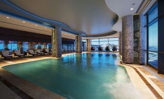 an indoor swimming pool surrounded by lounge chairs , where people are relaxing and enjoying their time at Shahdag Hotel & Spa