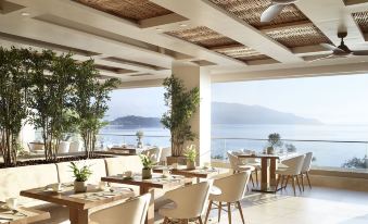 a restaurant with wooden tables and chairs , large windows offering views of the ocean , and ceiling fans at Ikos Dassia