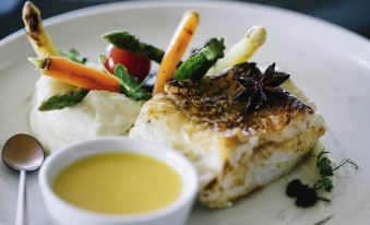 a plate of food with a white sauce , vegetables , and sauce is presented on a white plate at Raffles Seychelles