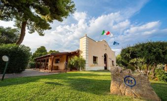 a stone building with a flag flying in front of it , surrounded by green grass and trees at TH Marina di Sibari - Baia Degli Achei Village