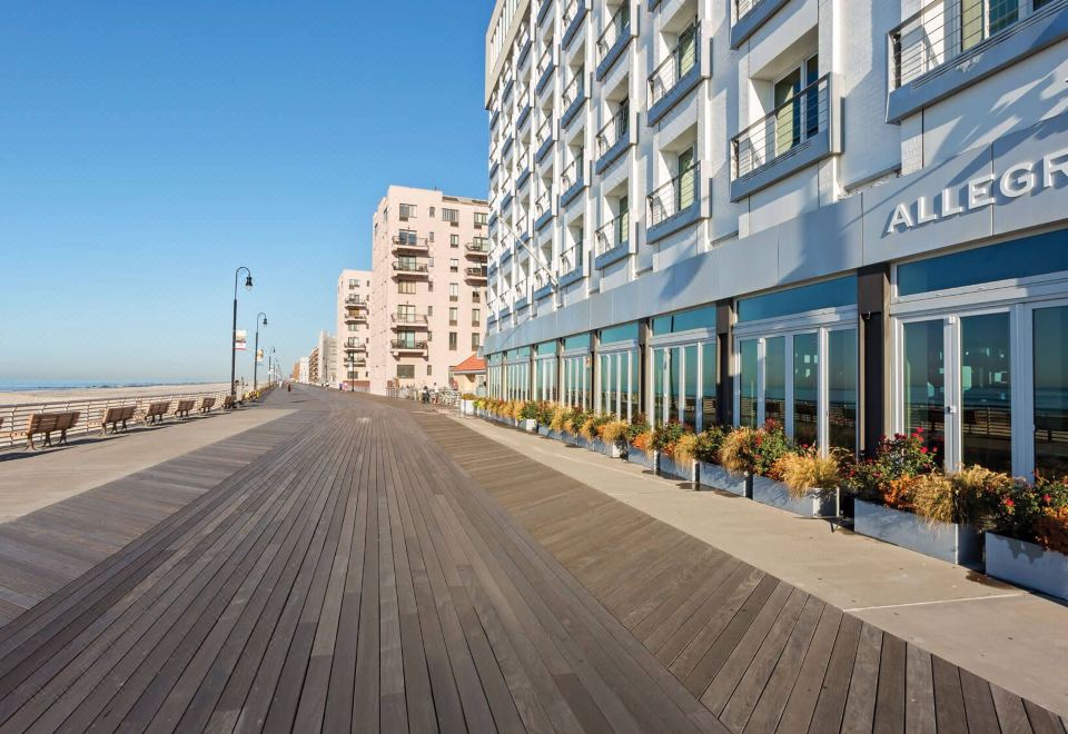 a wooden boardwalk with potted plants and buildings in the background , under a clear blue sky at Allegria Hotel