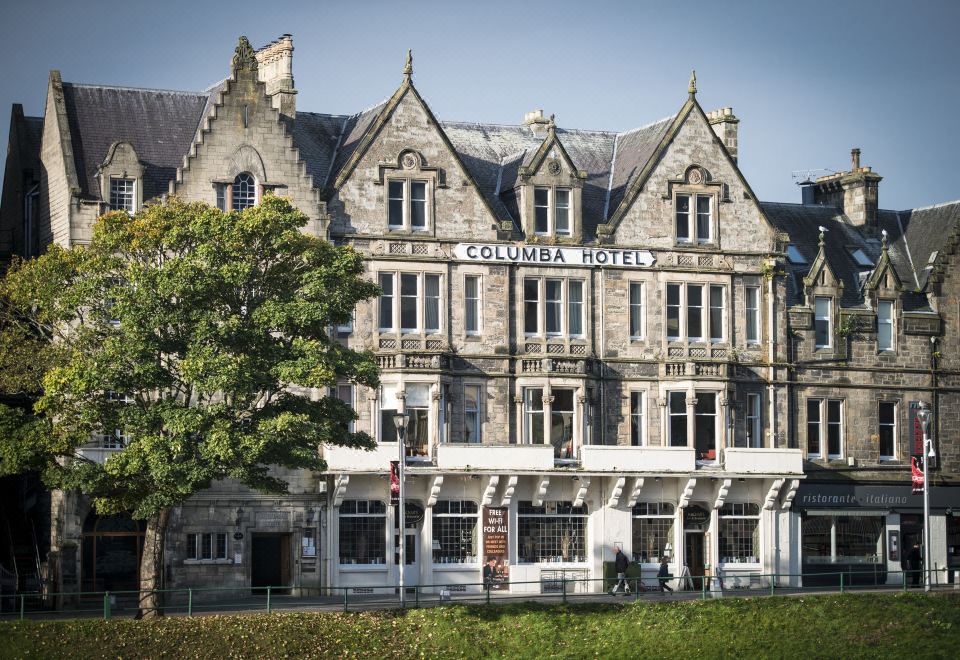 the exterior of the columbia hotel , a large stone building with multiple floors and balconies , surrounded by green grass and trees at Columba Hotel Inverness by Compass Hospitality