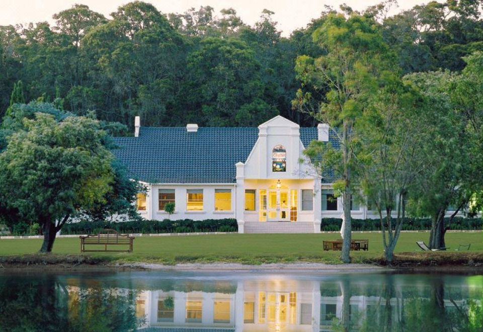 a white house with a blue roof and yellow lights is reflected in the water at Cape Lodge