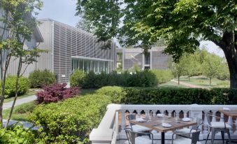 a restaurant patio with a dining table and chairs , surrounded by greenery and a building in the background at Topping Rose House