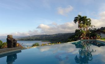 a large swimming pool with a palm tree in the foreground and mountains in the background at Hotel la Mansion Inn Arenal