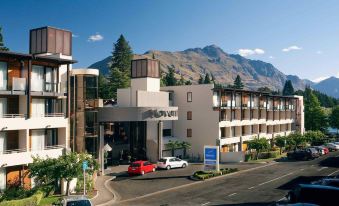 a modern building with a car parked in front and a mountain in the background at Novotel Queenstown Lakeside