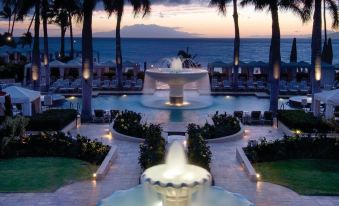 a beautiful resort with a large pool surrounded by palm trees , benches , and a fountain at Four Seasons Resort Maui at Wailea