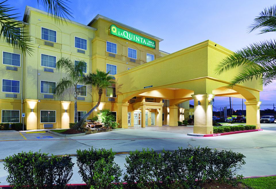 a large yellow and green hotel building with palm trees in front of it , under a clear blue sky at La Quinta Inn & Suites by Wyndham Houston Channelview