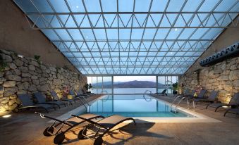 an indoor swimming pool surrounded by a glass ceiling , with lounge chairs placed around the pool area at Parador de Lorca