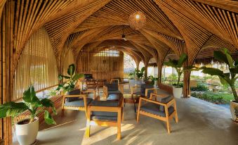 a room with wooden furniture , including chairs and tables , under a thatched roof , surrounded by greenery at Lahana Resort Phu Quoc & Spa