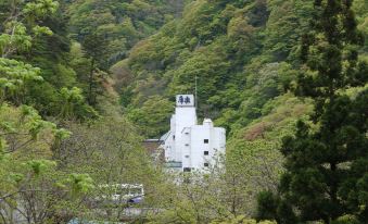 a large white building nestled in a lush green forest , surrounded by trees and mountains at Harataki