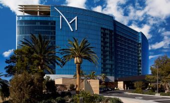 "a large blue building with a white letter "" m "" on the side , surrounded by palm trees and other greenery" at M Resort Spa & Casino